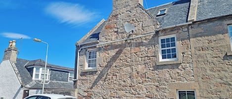 A white car parked in front of a stone building with multiple chimneys and a satellite dish.