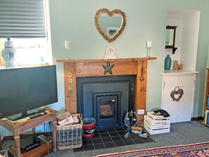 A living room with a fireplace, a television, a wicker basket, and a cabinet with a heart-shaped decoration. - 2 bedroom accommodation in Nairn (Nairn)