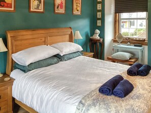 A neatly made bed with pillows, a bedside table with a lamp, a small table with a mirror, and a window with a view. - 2 bedroom accommodation in Nairn (Nairn)