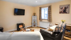A living room with a fireplace, a television, a sofa, a coffee table, and a window with curtains. - 1 bedroom accommodation in Llanfair Caereinion (Llanfair Caereinion)