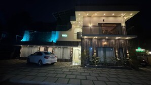 Een modern, tweelaags gebouw met een auto ervoor, een balkon en een goed verlichte ingang.