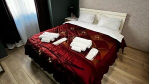 Un letto rifatto con ordine, con una coperta rossa, cuscini bianchi e asciugamani bianchi piegati con cura.