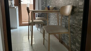 Zona pranzo con tavolo e sedie, parete in pietra e vista sugli edifici esterni.