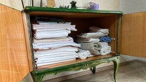 Un mobiletto in legno verde con ripiano in vetro, contenente asciugamani piegati e un piccolo oggetto decorativo.