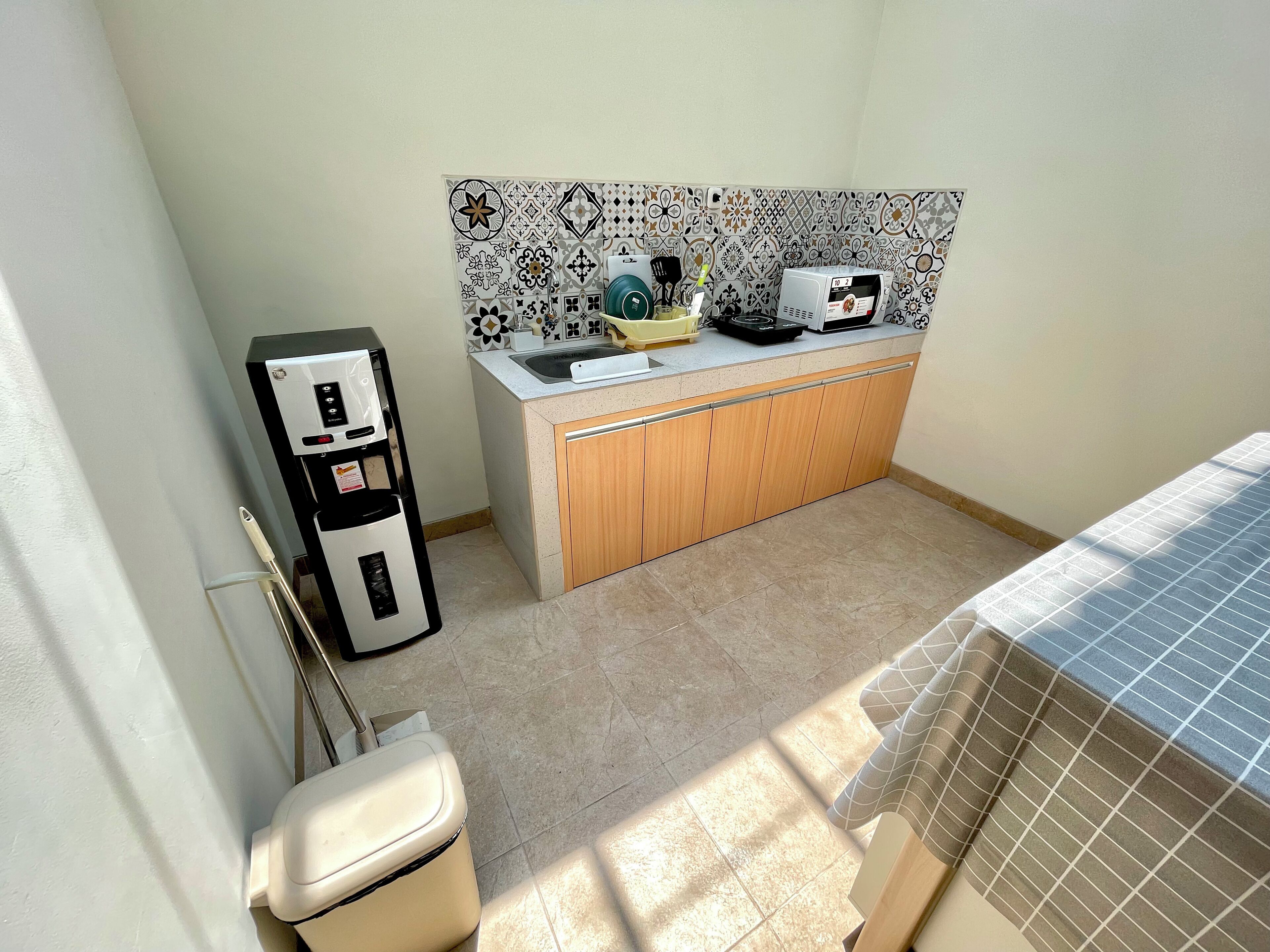 A compact kitchen with a refrigerator, microwave, sink, and patterned backsplash.