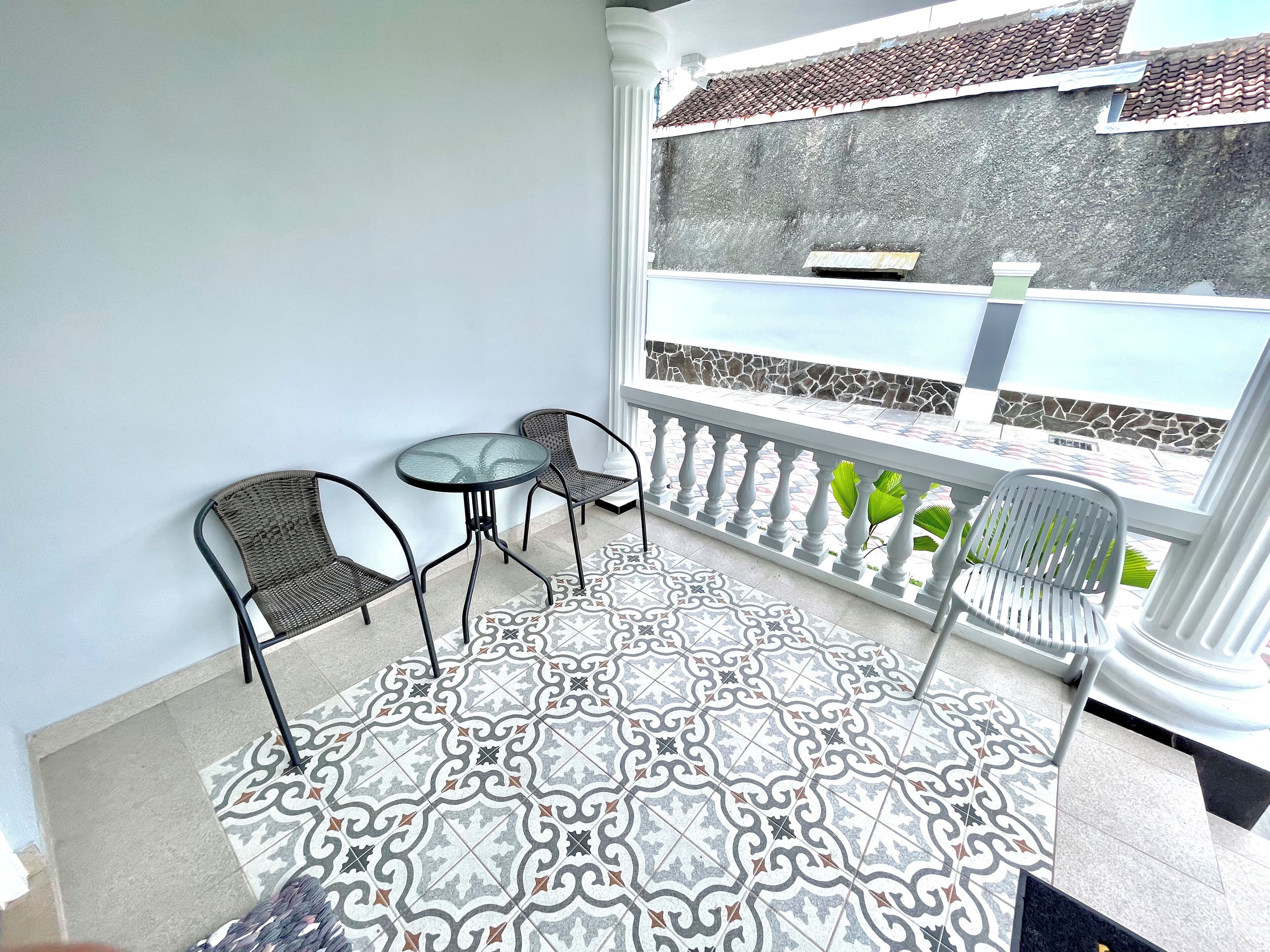 Un balcon doté d’un sol à motifs, d’une table, de deux chaises et offrant une vue sur un mur en pierre et des plantes.