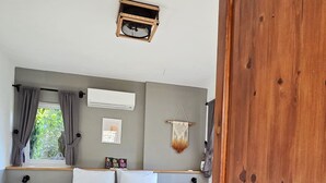 Une chambre à coucher comprenant un lit, des tables de chevet, une armoire en bois, un climatiseur fixé au mur et une fenêtre avec des rideaux.