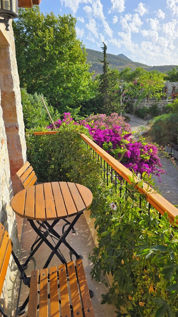 A wooden table and bench on a balcony with a view of a river and mountains.