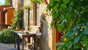 Un bâtiment en pierre avec une table et des chaises en bois à l’extérieur, des marches menant à l’entrée et de la verdure tout autour.