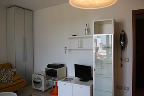 Ein modernes Zimmer mit Kleiderschrank, einem kleinen Tisch mit Computer, einer Glastruhe und einem Sofa.