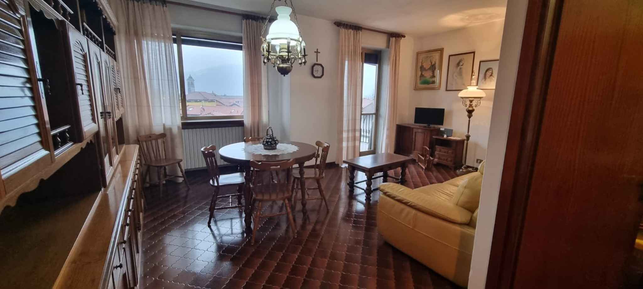 Zona pranzo con un tavolo rotondo e sedie, un divano, un lampadario e vista all'esterno.