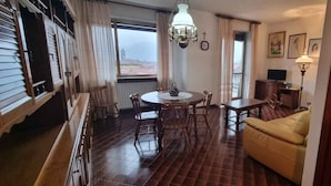 Een eetruimte met een ronde tafel en stoelen, een bank, een kroonluchter en uitzicht op buiten.