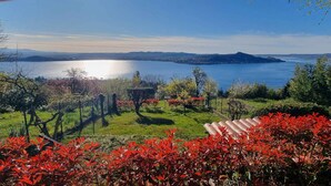 A scenic view of a lake with a distant mountain range, surrounded by lush greenery and red foliage. - Chalet with garden and lake view (Lesa Massino Visconti)