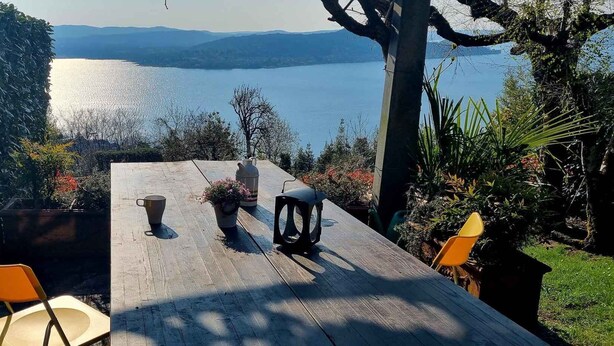 A wooden table with chairs, a potted plant, and a pitcher, overlooking a lake with mountains in the background. - Chalet with garden and lake view (Lesa Massino Visconti)