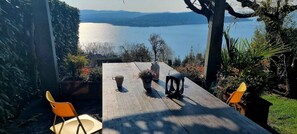 A wooden table with chairs, a potted plant, and a pitcher, overlooking a lake with mountains in the background. - Chalet with garden and lake view (Lesa Massino Visconti)