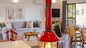 Un salon moderne avec une cheminée centrale, un canapé, une table à manger et un téléviseur fixé au mur.