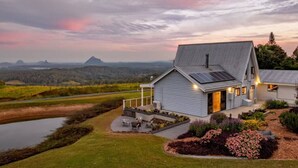 Une maison avec un toit en pente, des panneaux solaires, une véranda et une vue sur un lac et des montagnes.