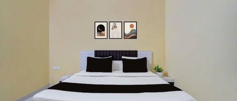 Una cama individual con colchón blanco y cabecera negra, una mesita de noche pequeña y un aire acondicionado instalado en la pared.
