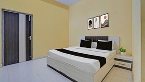 A bedroom with a bed, bedside tables, a nightstand, and wall art. - Hotel Sri Krishna Palace (Bhubaneshwar)