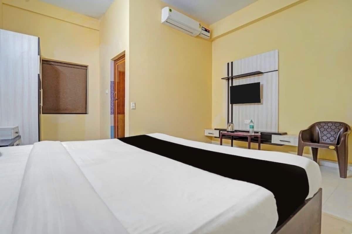 Una habitación de hotel con cama, escritorio, silla, unidad de aire acondicionado y televisión montada en la pared.
