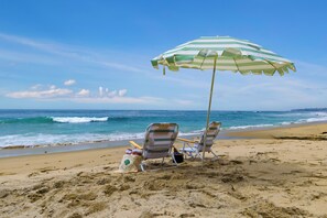 Une plage avec deux chaises de plage à rayures et un parasol à rayures vertes et blanches.