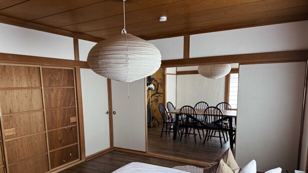 A bedroom with a bed, pillows, a wooden wardrobe, and a dining area with chairs and a table. - Rusutsu Tsuru House 2. (喜茂別町)