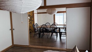 A traditional Japanese-style room with tatami flooring, a low wooden table with chairs, and a sliding door leading to a dining area. - Rusutsu Tsuru House 2. (喜茂別町)