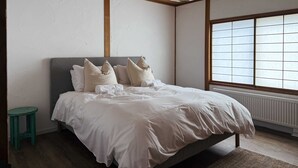 A bedroom with a bed, a small stool, a radiator, and a window with blinds. - Rusutsu Tsuru House 2. (喜茂別町)