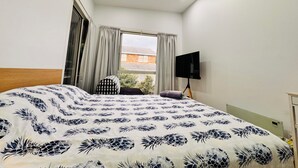 A bedroom with a bed, a TV, a window, and a view of a building outside.