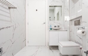 A modern bathroom with a white door, marble walls, a sink with a mirror, and a toilet.