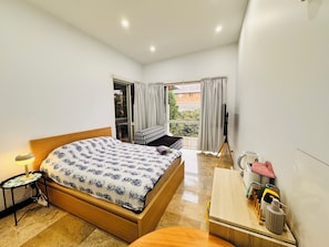 Un dormitorio con cama, mesita de noche, lámpara y vistas al exterior.
