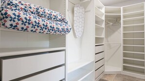 A walk-in closet with white shelving, a patterned cushion, and a geometric wall hanging.