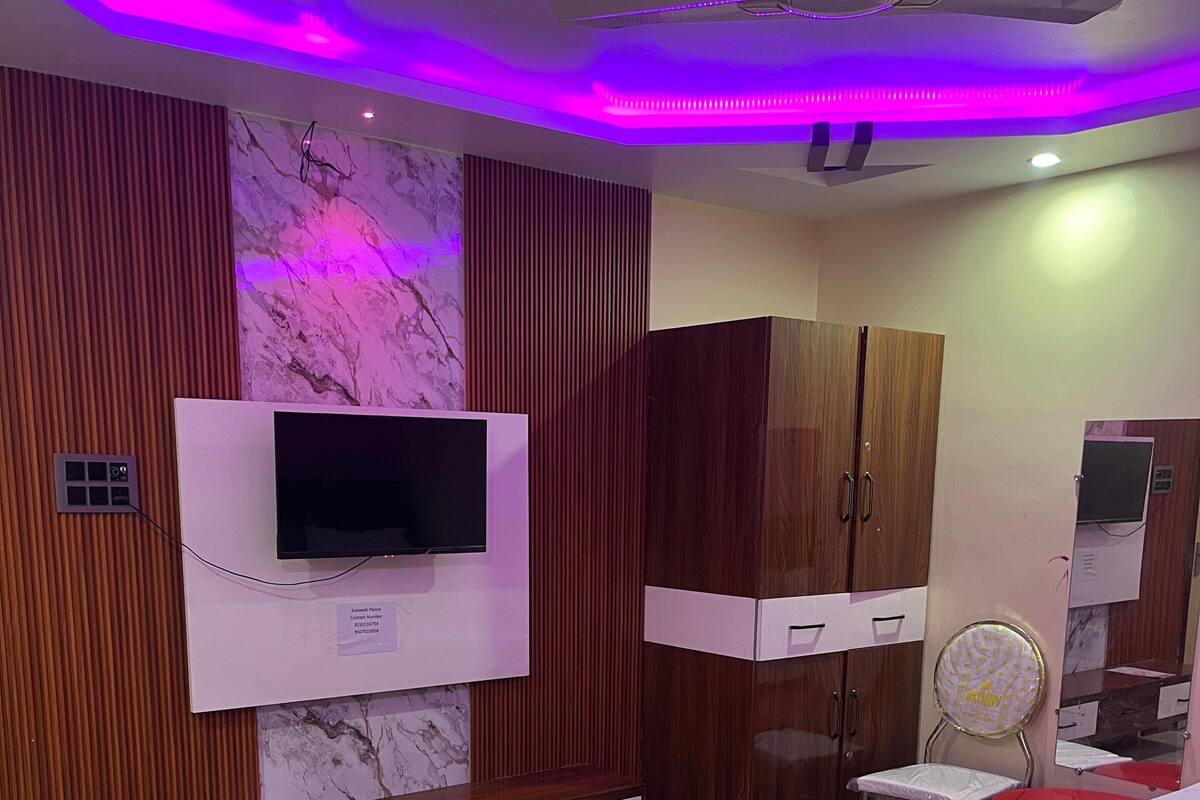 A bedroom with a bed, a TV mounted on a wooden cabinet, a vanity with a mirror, and a ceiling fan.