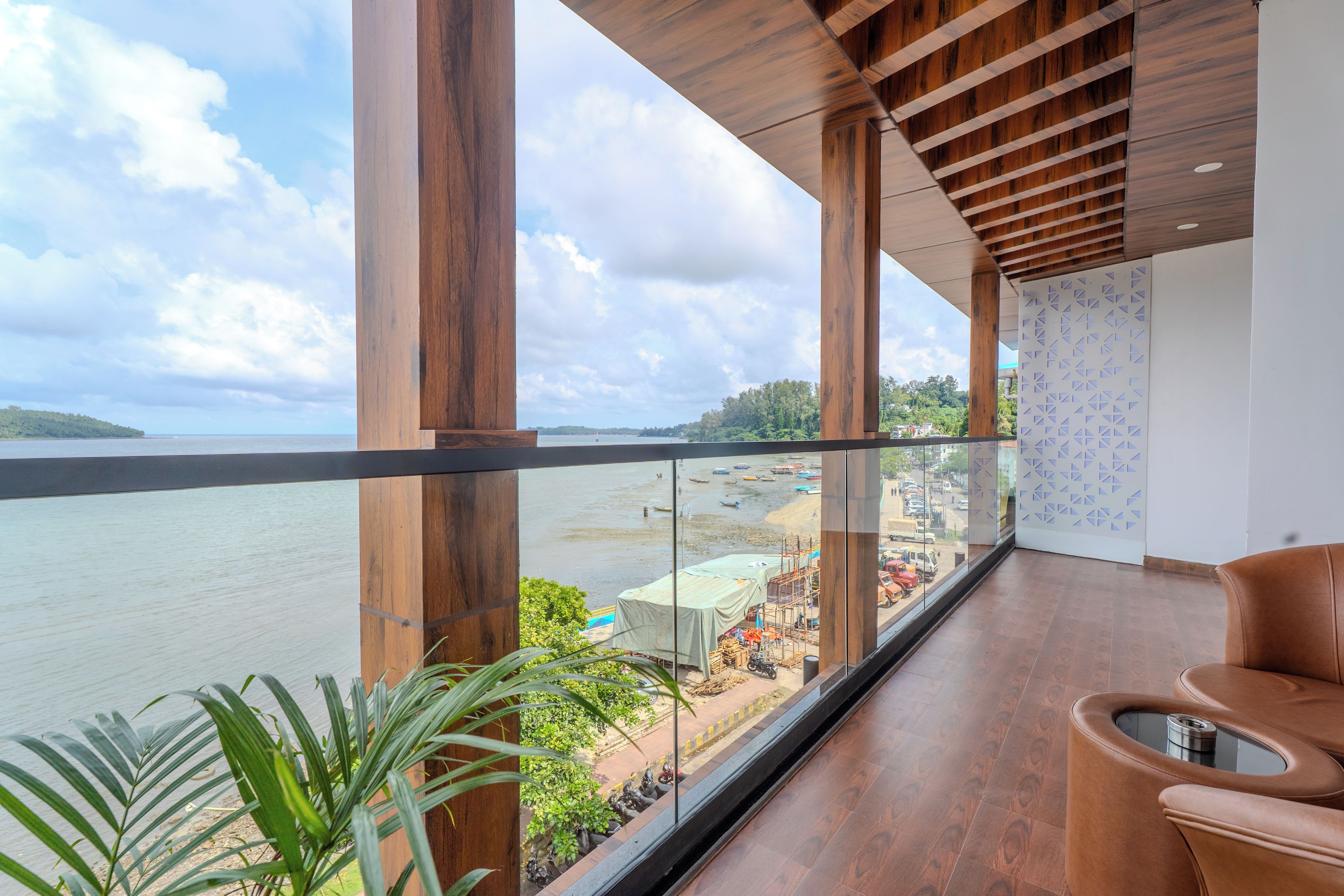 A balcony with a view of a river and boats, wooden pillars, a glass railing, and a brown leather chair.