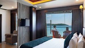 A hotel room with a bed, a television, a chair, and a view of the sea. - SEA BLISS (Port Blair)