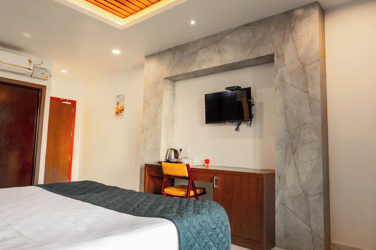 Habitación de hotel con cama, escritorio con silla, televisor montado en la pared y lámpara en el techo.