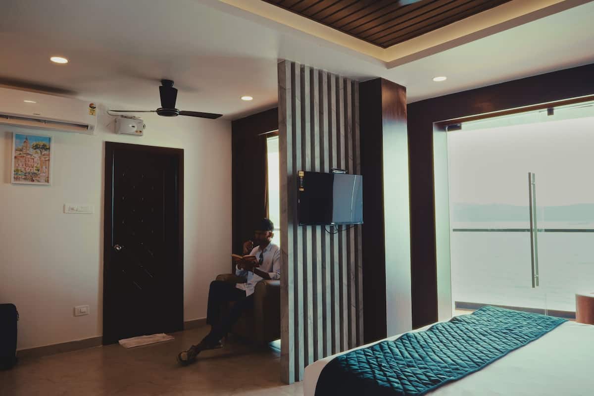 Una habitación de hotel moderna con cama, televisión, ventilador de techo y un amplio ventanal con vistas.
