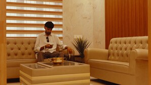 A man sitting on a sofa in a room with a large window, a plant, and a glass coffee table. - SEA BLISS (Port Blair)