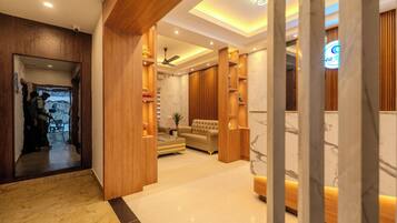 A modern interior with a wooden reception desk, a seating area with a sofa, and a marble floor.