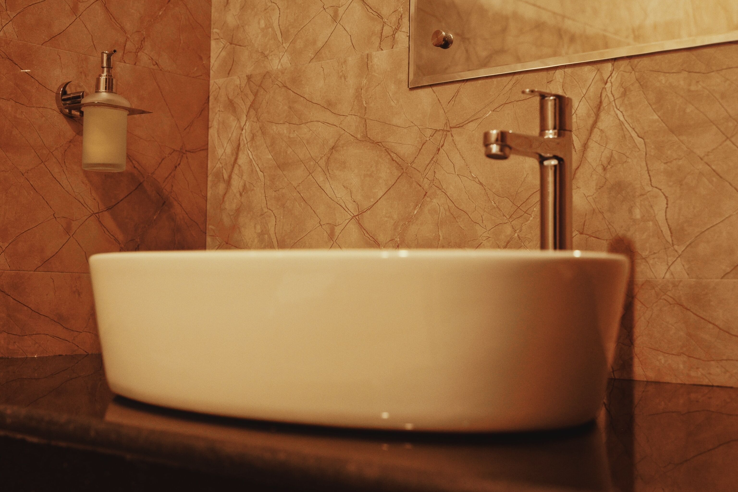 A bathroom with a white sink, a mirror, and a soap dispenser on the wall.