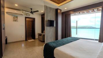 A hotel room with a bed, a chair, a TV, and a view of the sea.