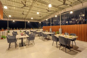 A spacious indoor dining area with multiple tables and chairs, ceiling fans, and a view of the night sky through a large window. - SEA BLISS (Port Blair)