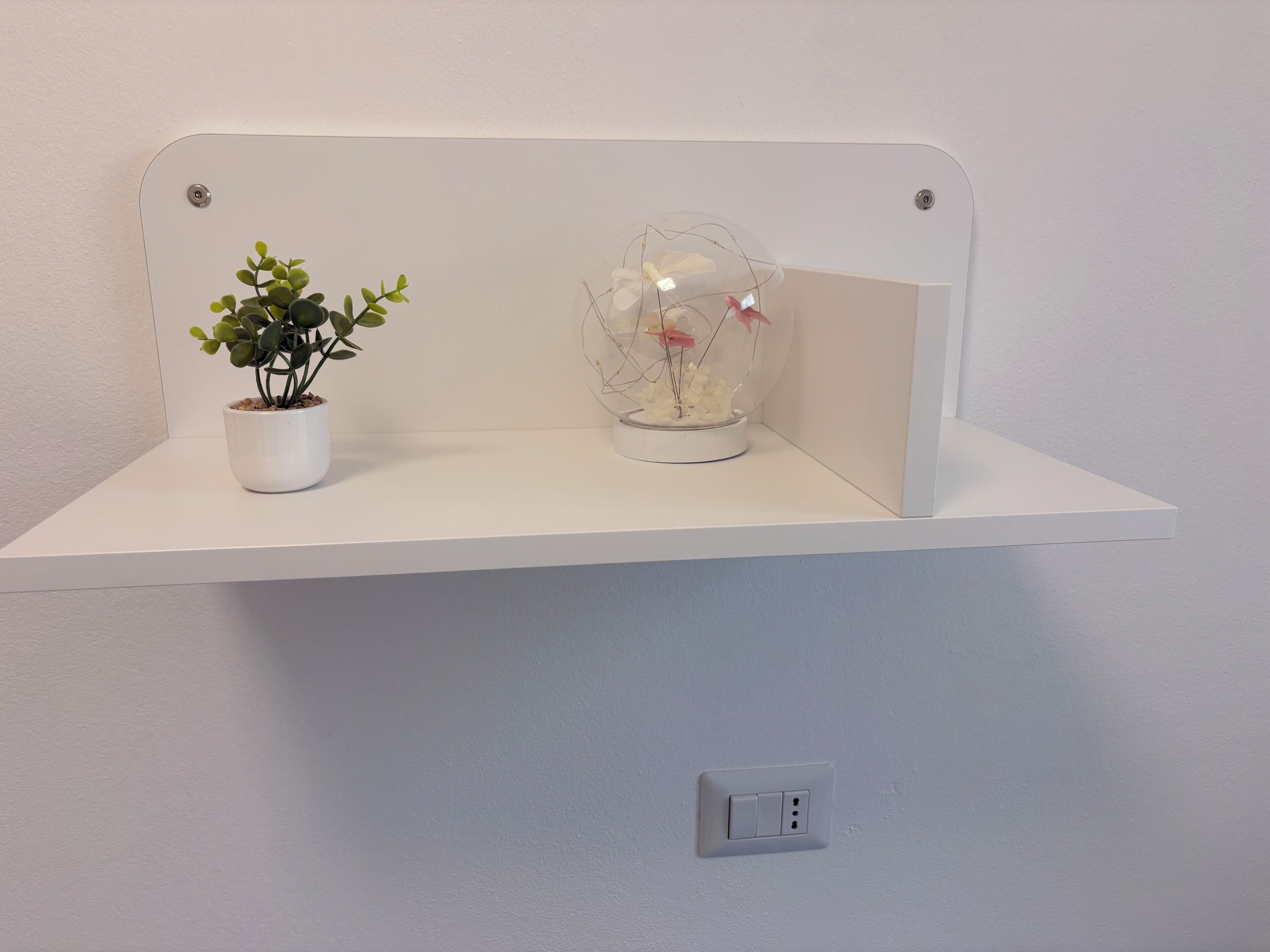 A white shelf with a potted plant and a decorative glass item.