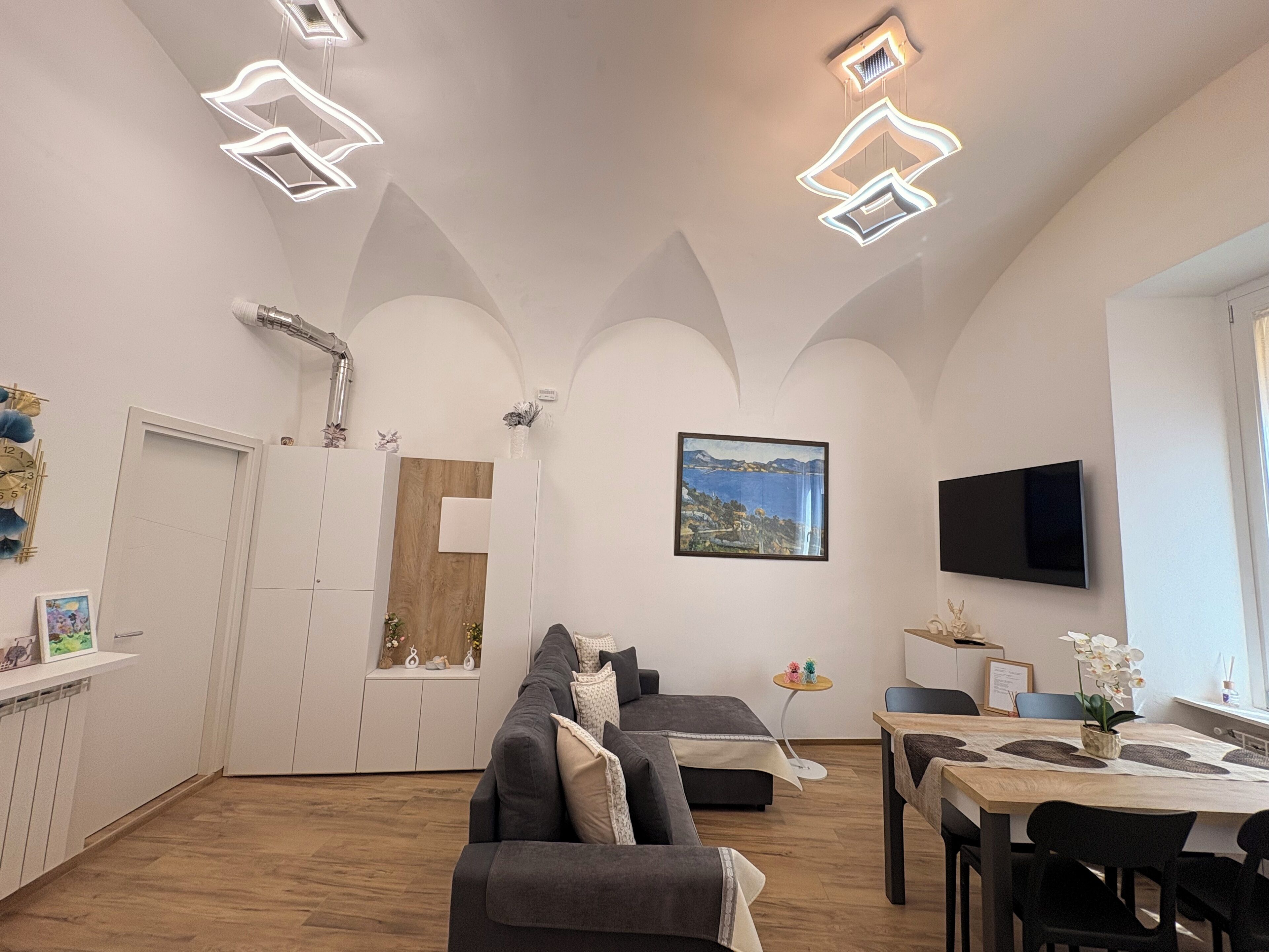 Een moderne woonkamer met een bank, een eettafel en een aan de muur bevestigde televisie.