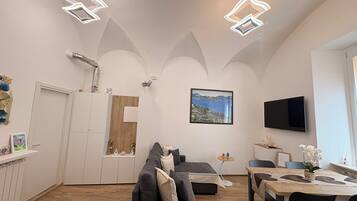 Een moderne woonkamer met een bank, een eettafel en een aan de muur bevestigde televisie.