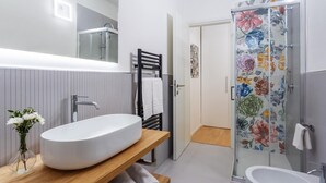 Ein modernes Badezimmer mit einem großem, ovalem Waschbecken, einer Duschkabine aus Glas mit floralen Mustern und einer separaten Badewanne.