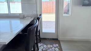 Una cocina moderna con encimera blanca, sillas negras, horno integrado y puerta que da a un patio trasero.