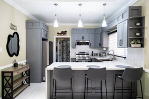 A modern kitchen with grey cabinetry, a central island with bar stools, and pendant lighting. - Clare's Manor in Ocho Rios with Mini Golf Course (Ocho Rios)
