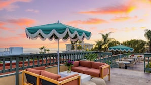 A rooftop terrace with outdoor seating, a view of the ocean, and a sunset sky. - Boutique Stay Near Beach | Pool + Hot Tub + Rooftop | Prime Laguna Location (Laguna Beach)