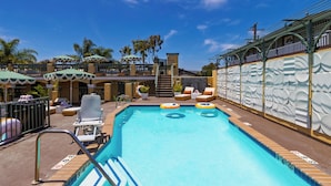 A swimming pool with lounge chairs and umbrellas, surrounded by palm trees and a building with a decorative facade. - Boutique Stay Near Beach | Pool + Hot Tub + Rooftop | Prime Laguna Location (Laguna Beach)